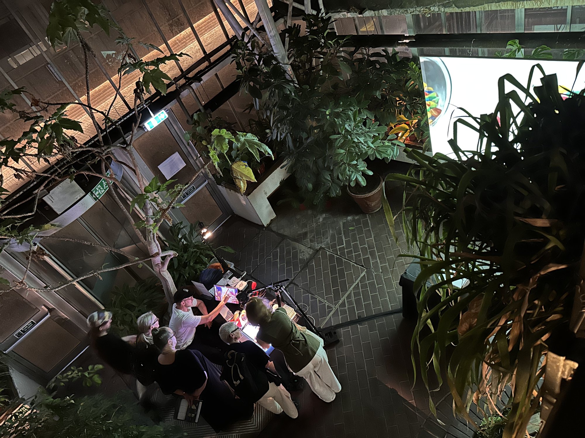 Looking down from a balcony onto a group of people gathered around the PromptTank table among the plants