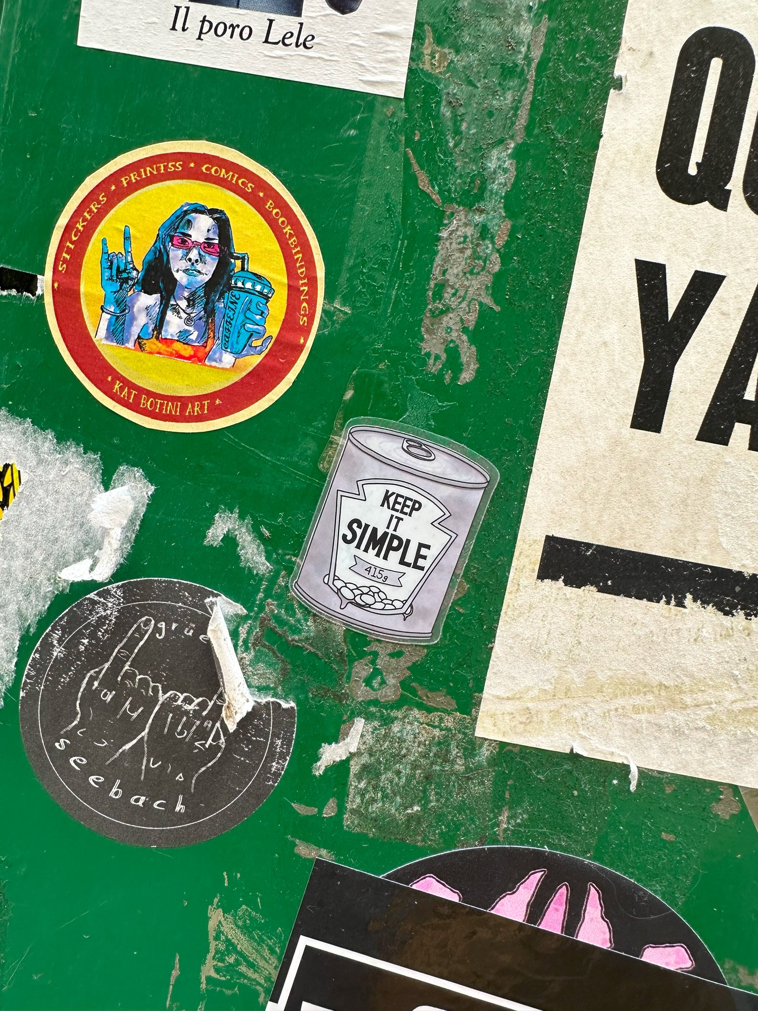 A Keep It Simple sticker on a green wall covered in posters and stickers
