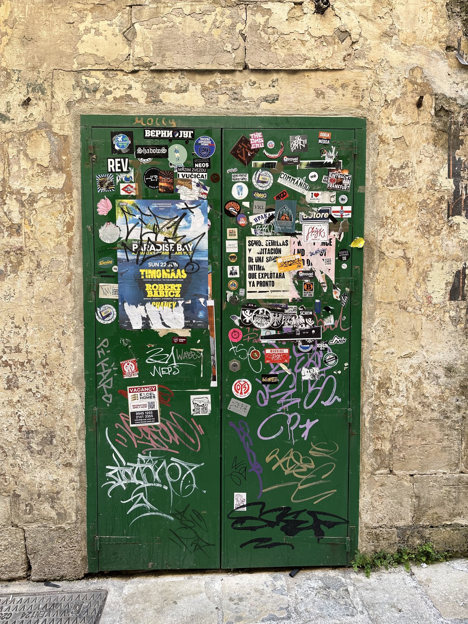 A green door in an old limestone wall, covered in stickers and graffiti