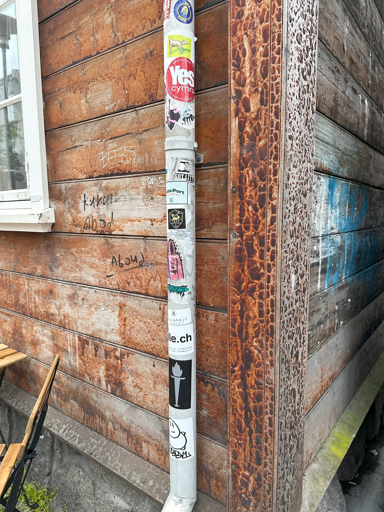 A sticker-covered pole against a weathered wooden building