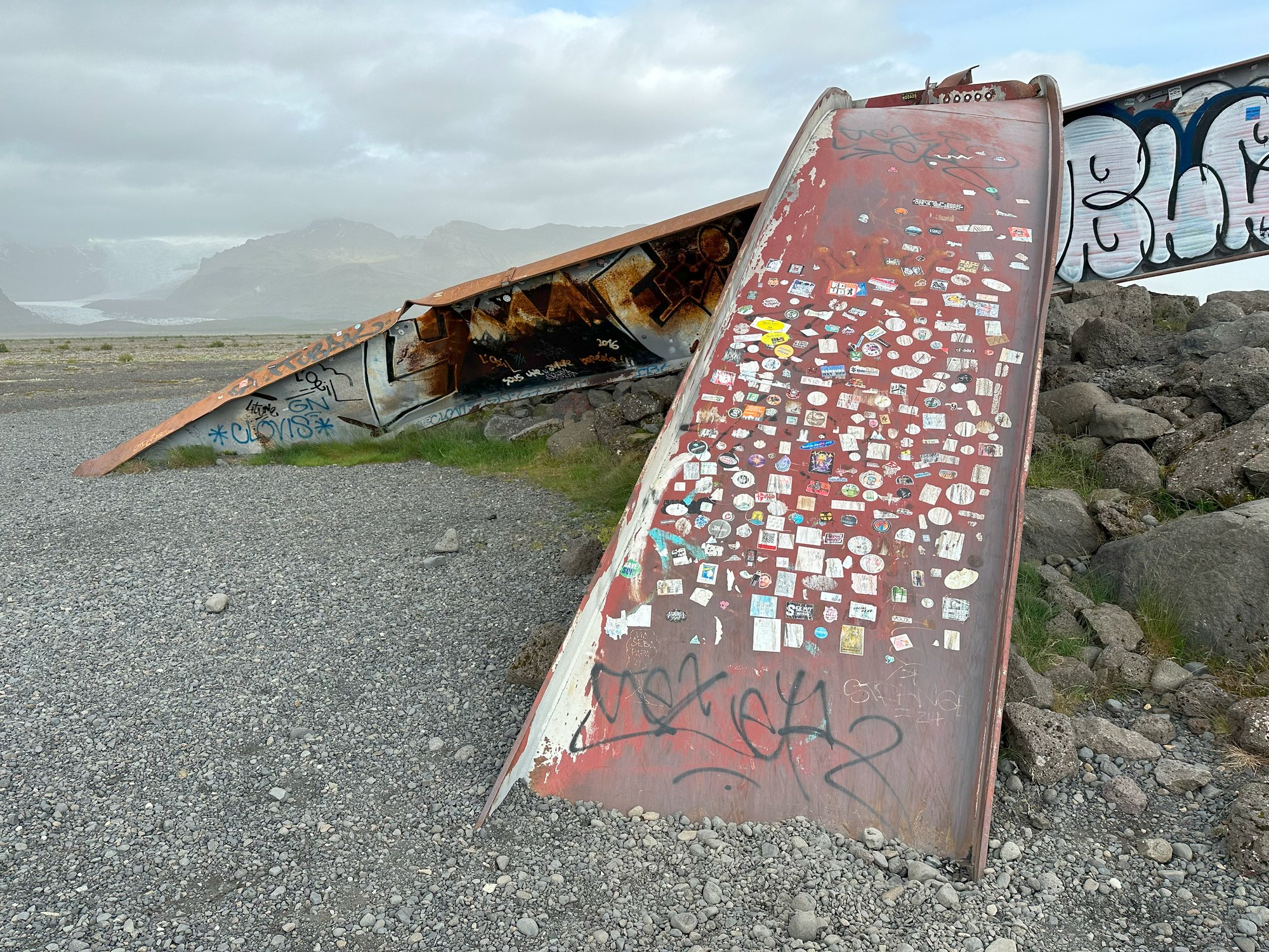 A sticker-covered metal slab leaning against rocks in a gravel landscape